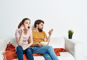 Fun man and energetic woman watching TV on the couch popcorn in a plate family communication