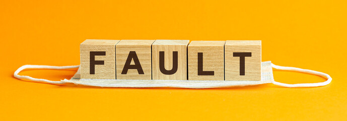 fault the word is written on wooden cubes lying on a medical mask. Concept. yellow background