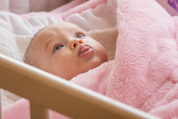 Four month old infant Caucasian woman lying in a pink wrap in a crib.
