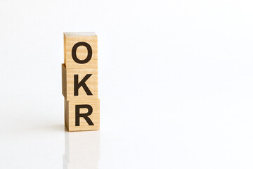Three wooden cubes with letters OKR - Objectives and Key Results, on white table, more in background, space for text in right down corner
