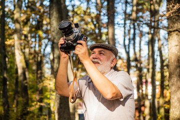 Fototapeta premium Best camera for professional. Old photographer on autumn day. Pensioner hold vintage camera in forest. Elderly man with photo camera. Using analog camera for shooting. Nature photo shoot session