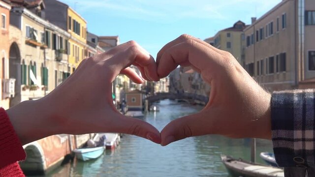 Male and female hands showing heart shape on the background of beautiful view of Venice. Symbol of love. Couple relationship, travel, family concept. Romantic picture of freedom.