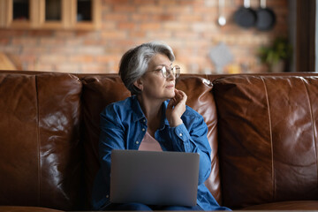 Thoughtful mature woman wearing glasses looking to aside, solving financial or health problems,...
