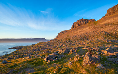 Sunlit rocky hill rising above a fjord and grassy slopes in Iceland