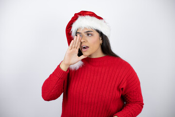 Young beautiful woman wearing a Santa hat over white background shouting and screaming loud to side with hand on mouth