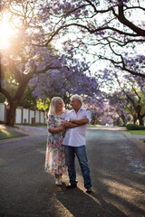 elderly man and woman walk down the street with blooming trees