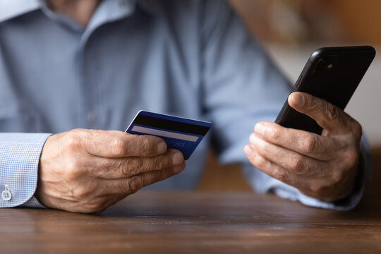 Close up senior man holding smartphone and plastic credit or debit card, mature customer paying online in store, entering information, browsing banking service, making secure internet payment
