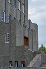 A striking modernist concrete building with tall narrow windows and an imposing tower stands in...