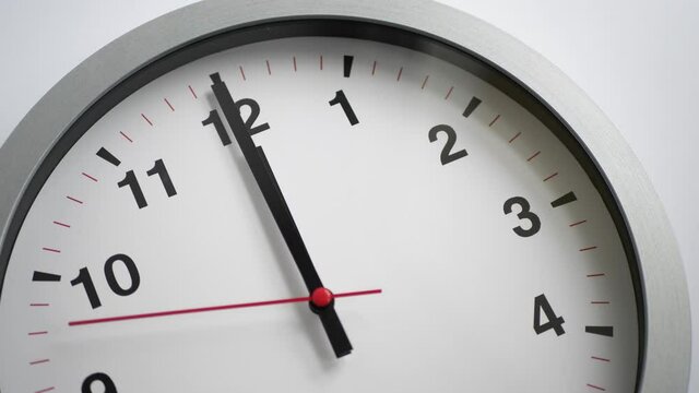 Close up of a white ticking clock on white background, pointing midnight
