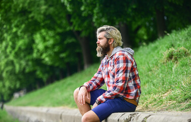 Naklejka na ściany i meble thoughtful hipster sit in park. enjoy nature this spring. male fashion style. he wear casual. brutal hipster with long beard and dyed hair. mature student relax outdoor. have a rest
