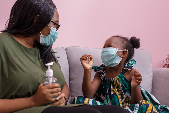 African Americans' Mother And Daughter Wearing A Mask Are Washing Their Hands With Alcohol To Protect Them From Germs And COVIC 19 While Staying At Home. Black People Or African Americans