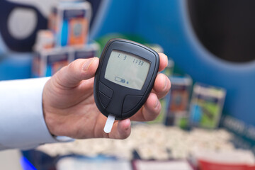 The hand holds a glucose meter with a test strip on an unfocused background. The concept of diabetes prevention.
