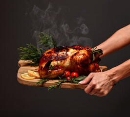 Woman hands hold plate with cooked thanksgiving turkey or chicken for christmas dinner evening with steam smoke on wooden rustic plate garnished with cherry berries and fruits on dark background