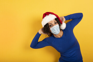Fototapeta na wymiar Happy woman with Christmas hat and face mask to be protect against covid-19. Yelow background