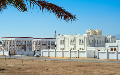 White fortress-like houses with crenellated walls and palm trees lining a street in Sur, Oman.