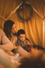 Little boy and mum reading children's story in his teepee room.