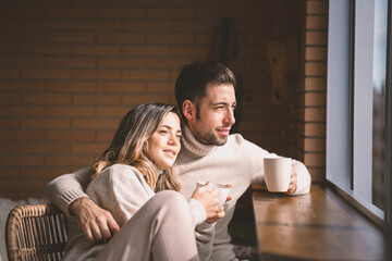 Young couple in love enjoying coffee on a sunny winter sunday morning by the window at home