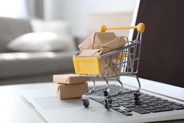 Internet shopping. Laptop and small cart with boxes on table indoors