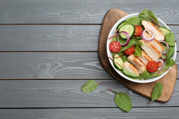 Delicious salad with chicken and vegetables on grey wooden table, flat lay. Space for text