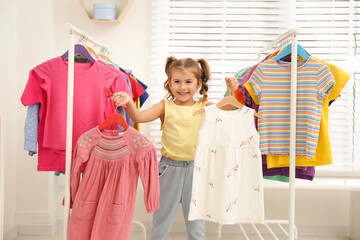 Little girl choosing clothes on racks indoors