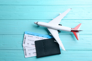 Toy airplane and passport with tickets on light blue wooden background, flat lay