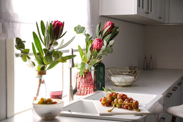 Vases with beautiful protea flowers near sink in kitchen. Interior design