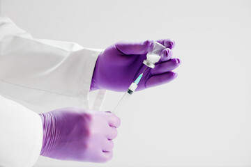 doctor with vaccine and syringe in hands, lilac surgical gloves, white background.