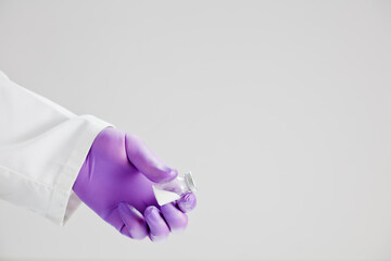 Vaccine in hand of doctor with surgical gloves, white background.