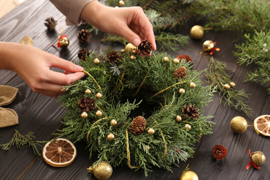 Florist making beautiful Christmas wreath at wooden table indoors, closeup