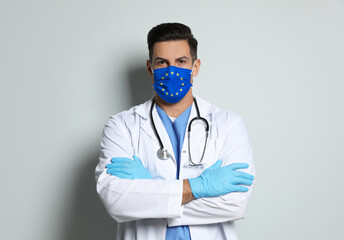 Doctor wearing medical mask with European Union flag on light background. Coronavirus outbreak in Europe