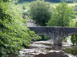 view of the historic packhorse bridge in the town of hebden bridge in west yorkshire surrounded by summer trees