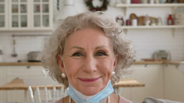 Nice retired woman with short hair lowers protective facial mask and smiles gently posing for camera closeup slow motion