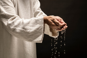 Water for Baptism pouring out of the hands of Jesus Christ during a dark night.