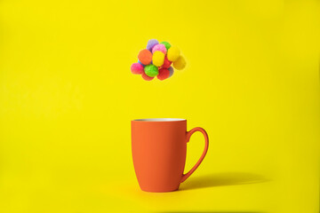 Colorful pom pom cloud above orange mug on yellow background