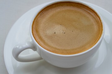 Artistic composition in natural light. Large white cup of hot coffee. Focus on the bubbles in the crema