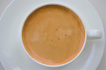 Artistic composition in natural light. Large white cup of hot coffee. Focus on the bubbles in the crema