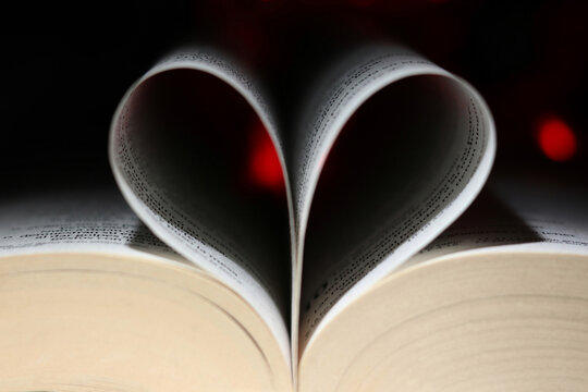 Pages of a book curved into a heart shape with dark background and red lights and bokeh