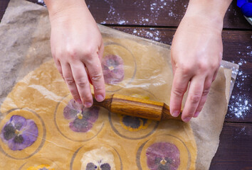 The chef's hands press the pansy flowers against the dough pieces through a sheet of baking paper...