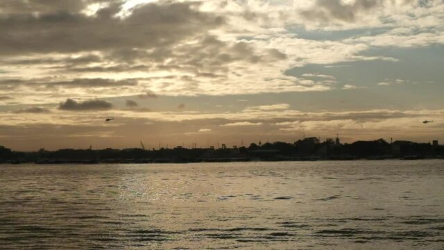 Two Helicopters flying over a city during a beautiful sunrise facing the sea  in the Philippines. No people.