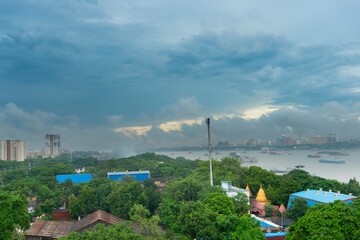 View of Howrah city from top. Green trees in foreground covering factories, holy river Ganges with floating boats in midground and skyline of Kolkata under blue sky in the horizon.Howrah city image.