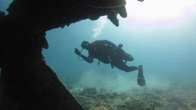 Scuba diver observing crane wreck up-close for coral growth.