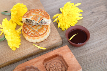 Obraz na płótnie Canvas Mid-autumn moon cakes and a bowl of tea, golden chrysanthemums and wooden moon cake molds are scattered on the table