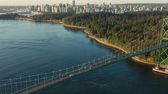 Drone Aerial Intro Shot of the  Lions Gate Bridge in Vancouver, Canada. with Skyline in the background and Peaking Sun