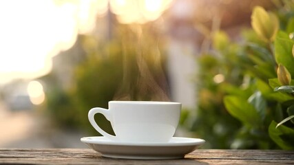 Close-up steaming hot coffee or tea cup on saucer, slow motion. Hot ceramic white coffee cup with smoke on old wooden table in nature background. Hot Coffee Drink Concept - Powered by Adobe