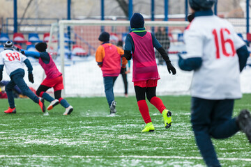 Obraz premium Boys in white sportswear running on soccer field with snow on background. Young footballers dribble and kick football ball in game. Training, active lifestyle, sport, children winter activity