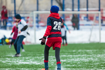 Obraz premium Boys in white sportswear running on soccer field with snow on background. Young footballers dribble and kick football ball in game. Training, active lifestyle, sport, children winter activity
