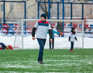 Boys in white sportswear running on soccer field with snow on background. Young footballers dribble and kick football ball in game. Training, active lifestyle, sport, children winter activity