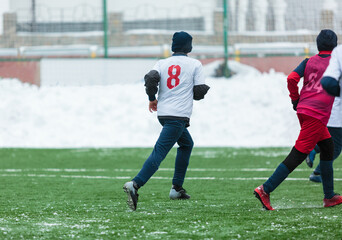 Boys in white sportswear running on soccer field with snow on background. Young footballers dribble...