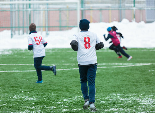 Boys in white sportswear running on soccer field with snow on background. Young footballers dribble and kick football ball in game. Training, active lifestyle, sport, children winter activity
