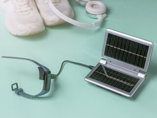 The smart watch is charged from a portable charger on the background of sneakers and headphones. Use of solar energy.